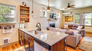 A spacious kitchen with granite countertops, a built-in sink, and wooden cabinets. There is a dining area with a table and chairs, and a living room with a sofa and a fireplace. - Charming Donnelly Home - 1 Mi to Lake Cascade! (Donnelly)
