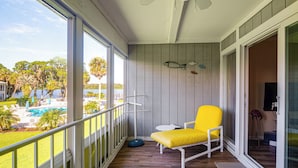 Un balcon avec une chaise jaune, une petite table et une vue sur une piscine et des palmiers.
