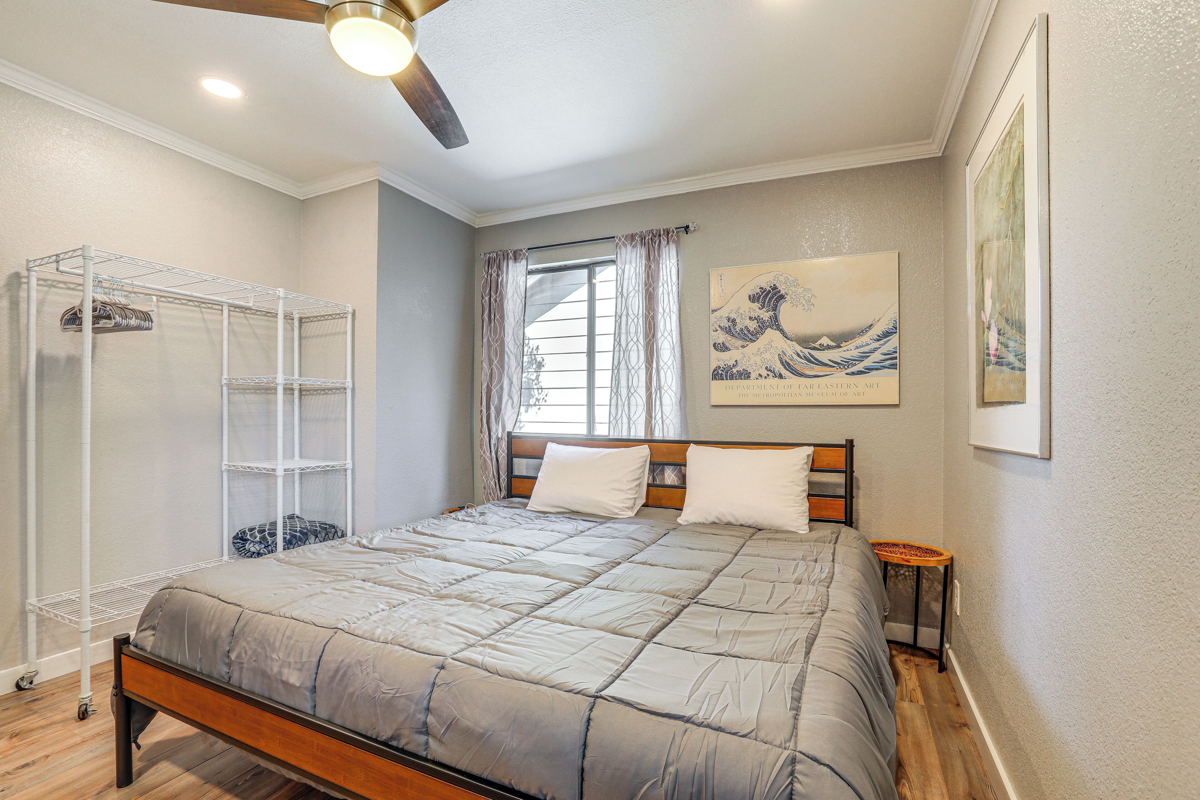 A bedroom with a bed, a ceiling fan, a window with curtains, a wall-mounted shelf, and artwork.
