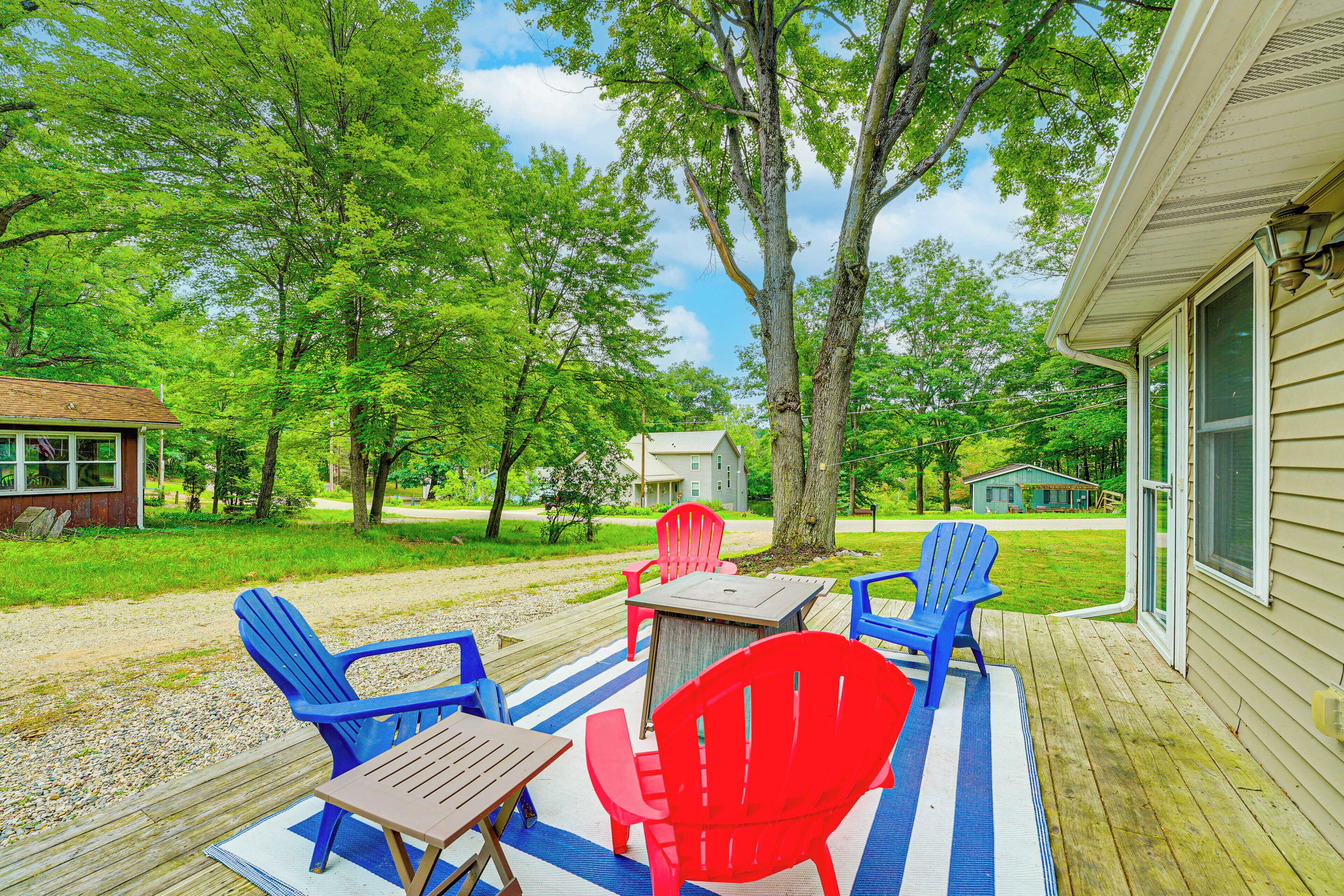 A wooden deck with a table and chairs, surrounded by trees and a house in the background.