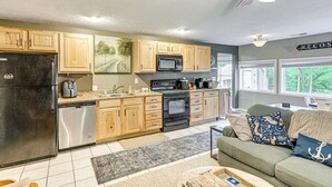 A modern kitchen with wooden cabinets, a refrigerator, dishwasher, microwave, and stove. There is a window with a view of trees and a ceiling fan with lights. - 2 MI to the Lake: Mecosta Getaway With Fire Pit! (Mecosta)