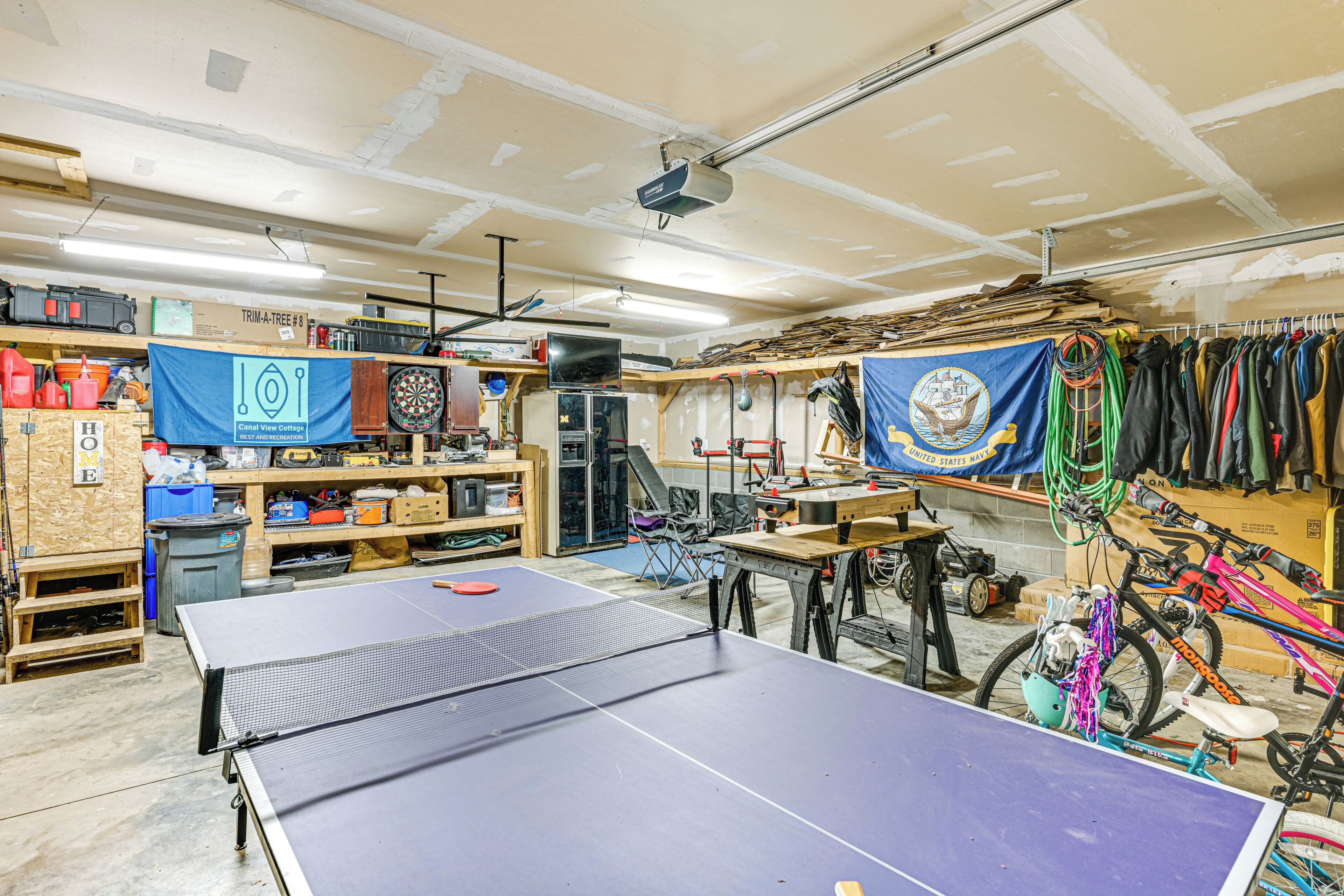 Una habitación con mesa de ping pong, estantes con objetos varios, dardo y una bicicleta.