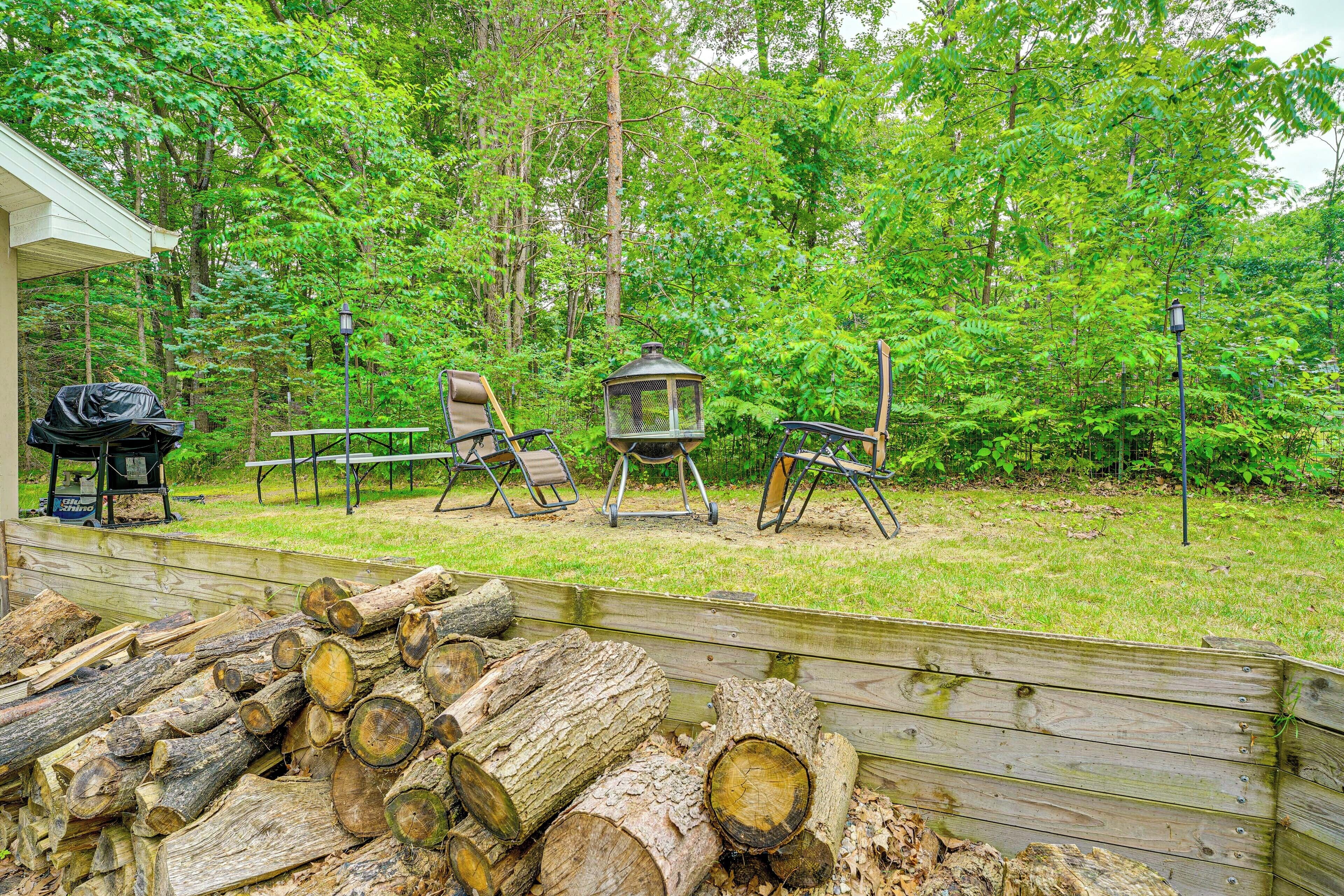 A deck with outdoor seating, a grill, and a pile of logs.