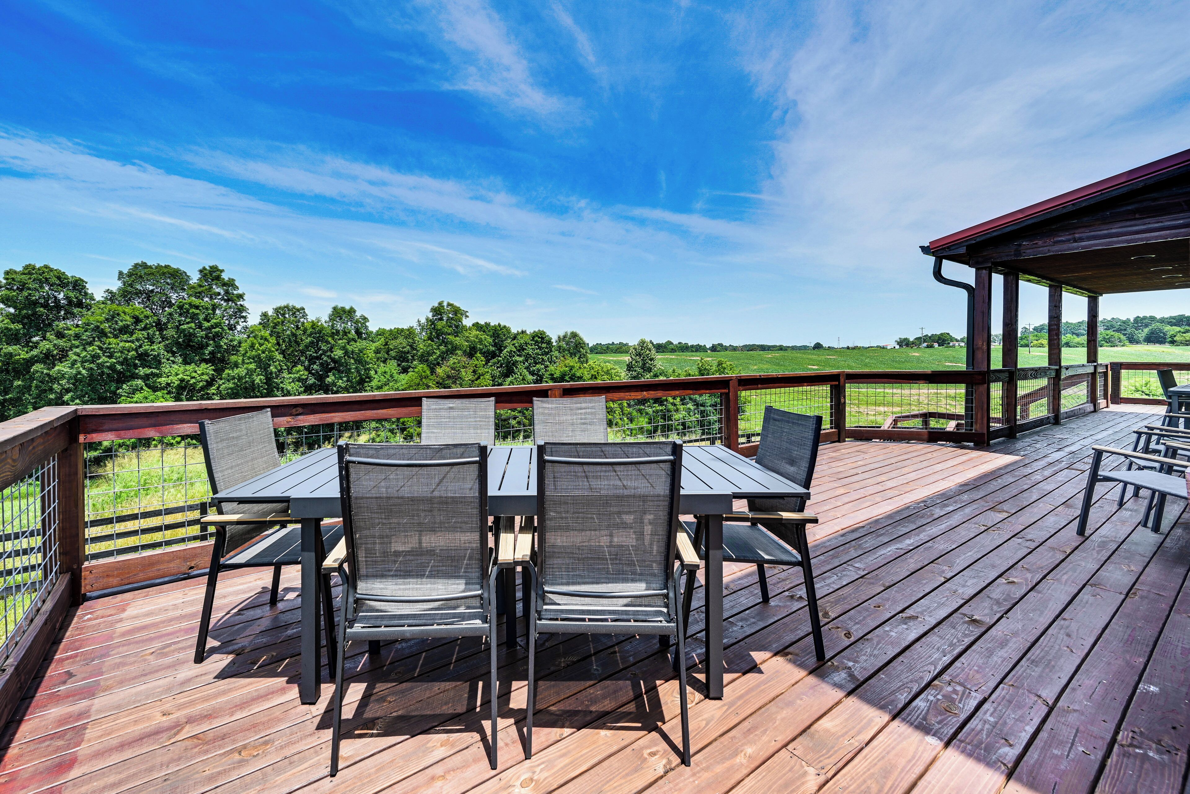 A wooden deck with outdoor furniture, a covered area, and a view of a green landscape.