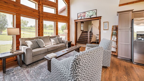 A spacious living room with a large window, a sofa, a patterned armchair, a coffee table, and a refrigerator. - Scenic Getaway w/ Deck: 7 Mi to Mammoth Cave Park! (Brownsville)