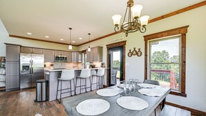 A spacious kitchen with a large island, stainless steel appliances, and a dining area with a long table and bar stools. - Scenic Getaway w/ Deck: 7 Mi to Mammoth Cave Park! (Brownsville)