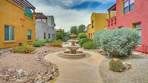 Un patio con una fuente central, rodeado de edificios de estilos arquitectónicos variados y diversas plantas desérticas.