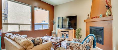 A living room with a sofa, armchair, coffee table, TV, fireplace, and large windows.