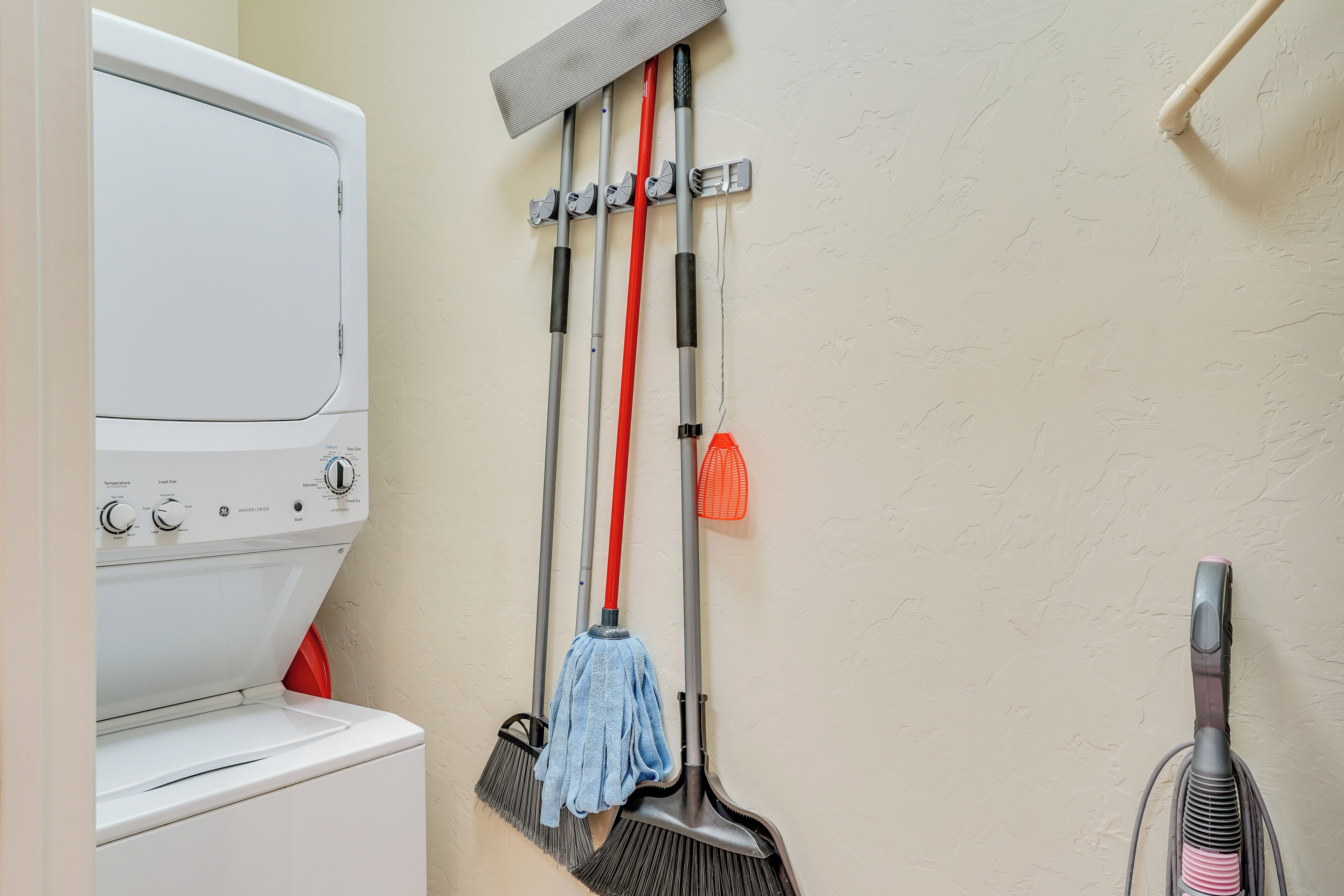 A laundry area with a washing machine, brooms, a mop, and a vacuum cleaner.