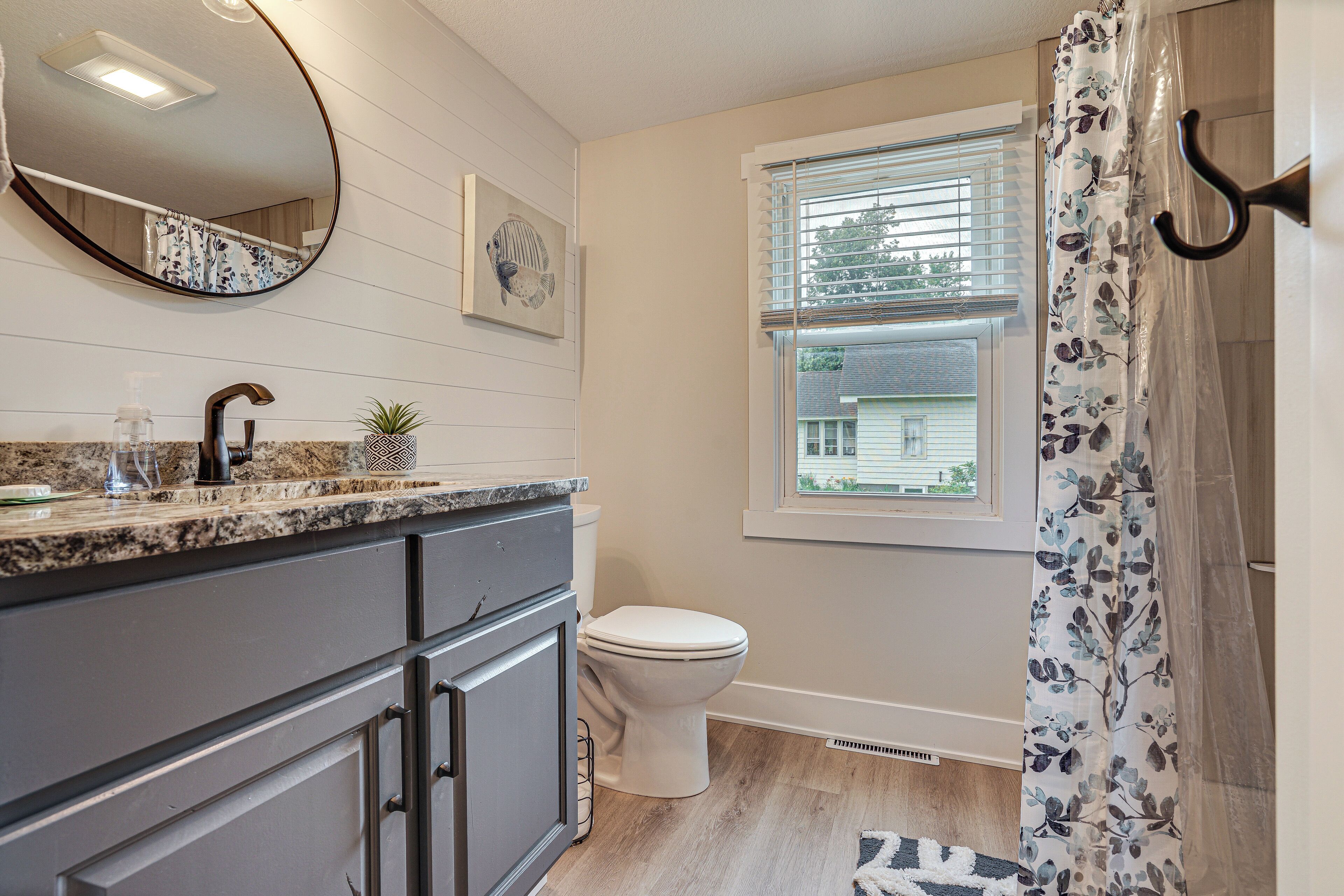 A bathroom with a toilet, sink, mirror, and window.