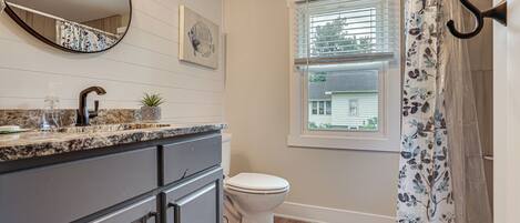 A bathroom with a toilet, sink, mirror, and window.