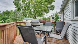 Een houten terras met een tafel, stoelen, een barbecue en een huis op de achtergrond.