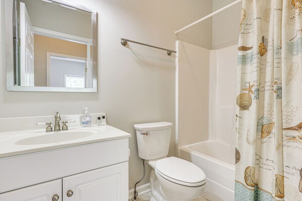 Une salle de bain avec un lavabo, des toilettes et une baignoire, tous de couleur blanche. On trouve un porte-serviettes au-dessus de la baignoire et un miroir au-dessus du lavabo.