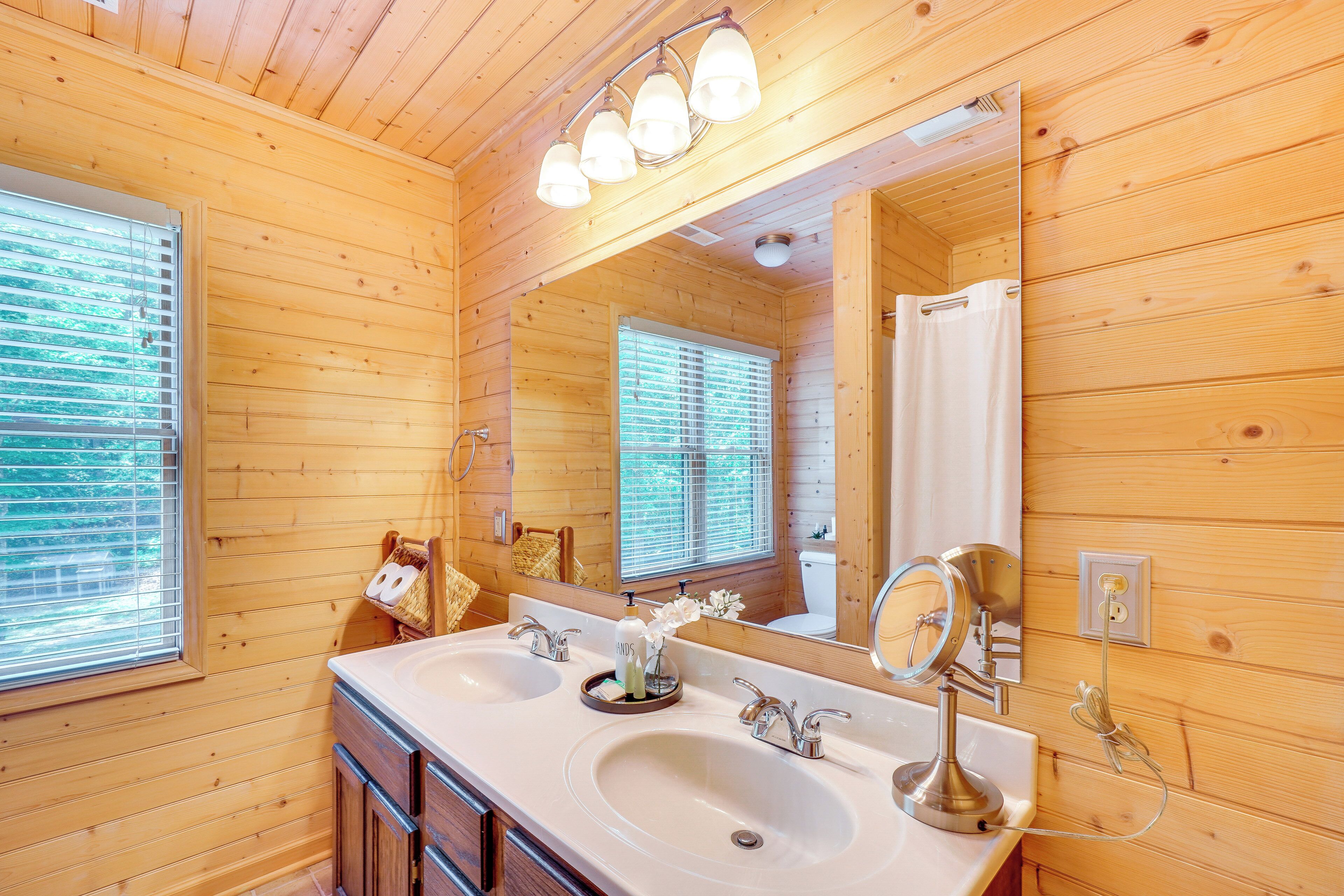 A wooden cabin bathroom with two sinks, a large mirror, and a ceiling light fixture.