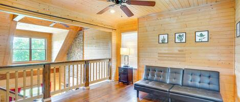 Una habitación amplia con techo de madera, un sofá de cuero negro, piso de madera y un ventilador de techo.