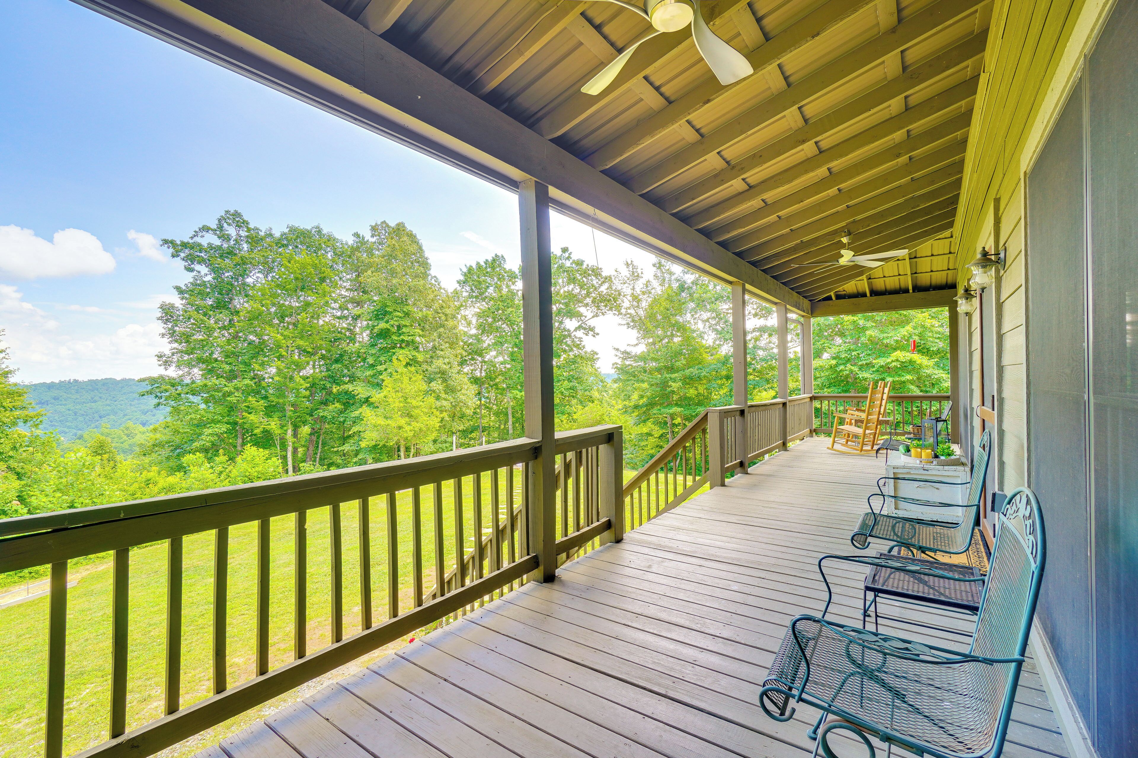 A covered porch with wooden railings, a ceiling fan, and outdoor seating.