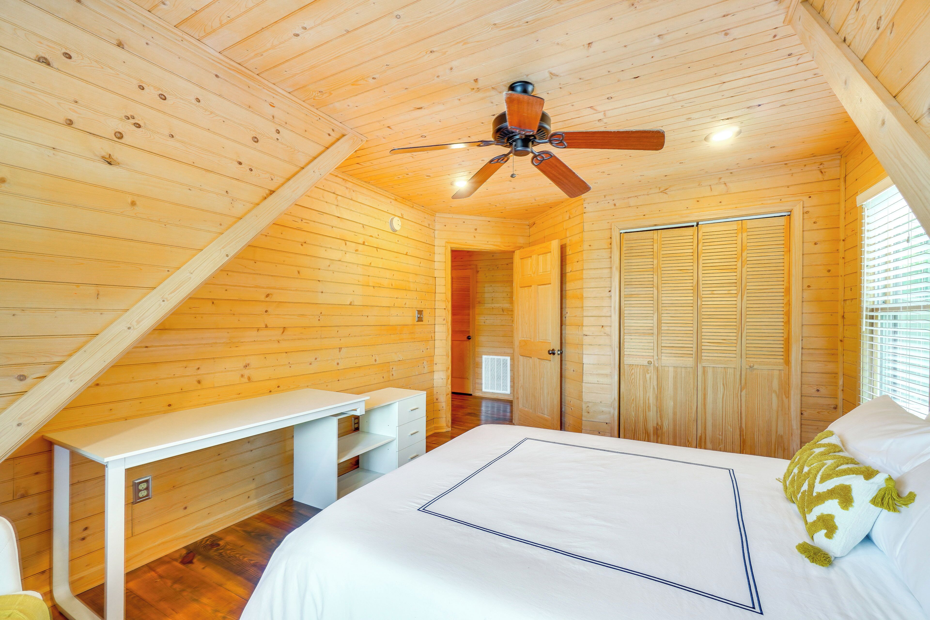 Un dormitorio con cama, escritorio, ventilador de techo y paredes de madera.