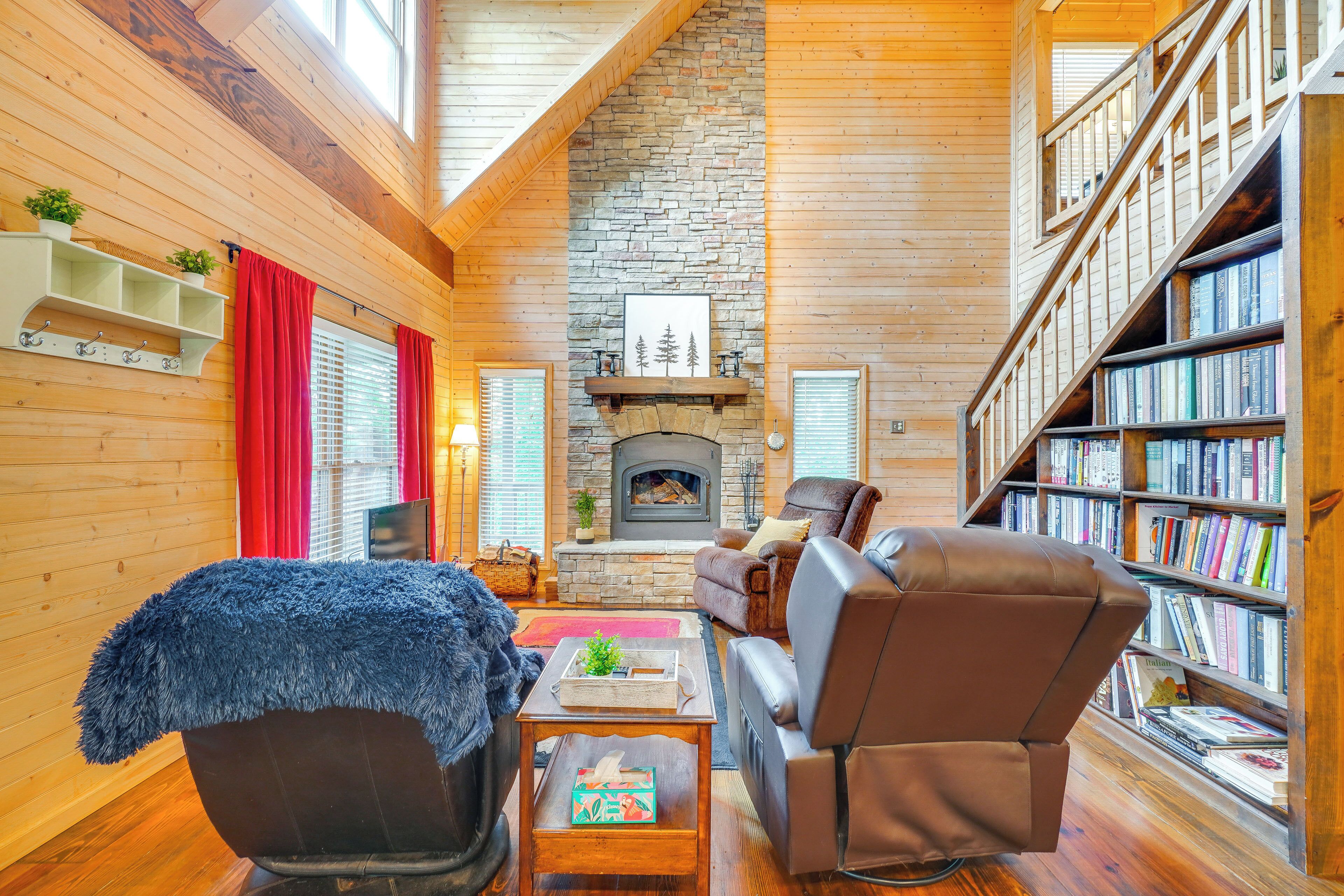 A cozy log cabin interior with a stone fireplace, leather recliner, and a bookshelf filled with books.