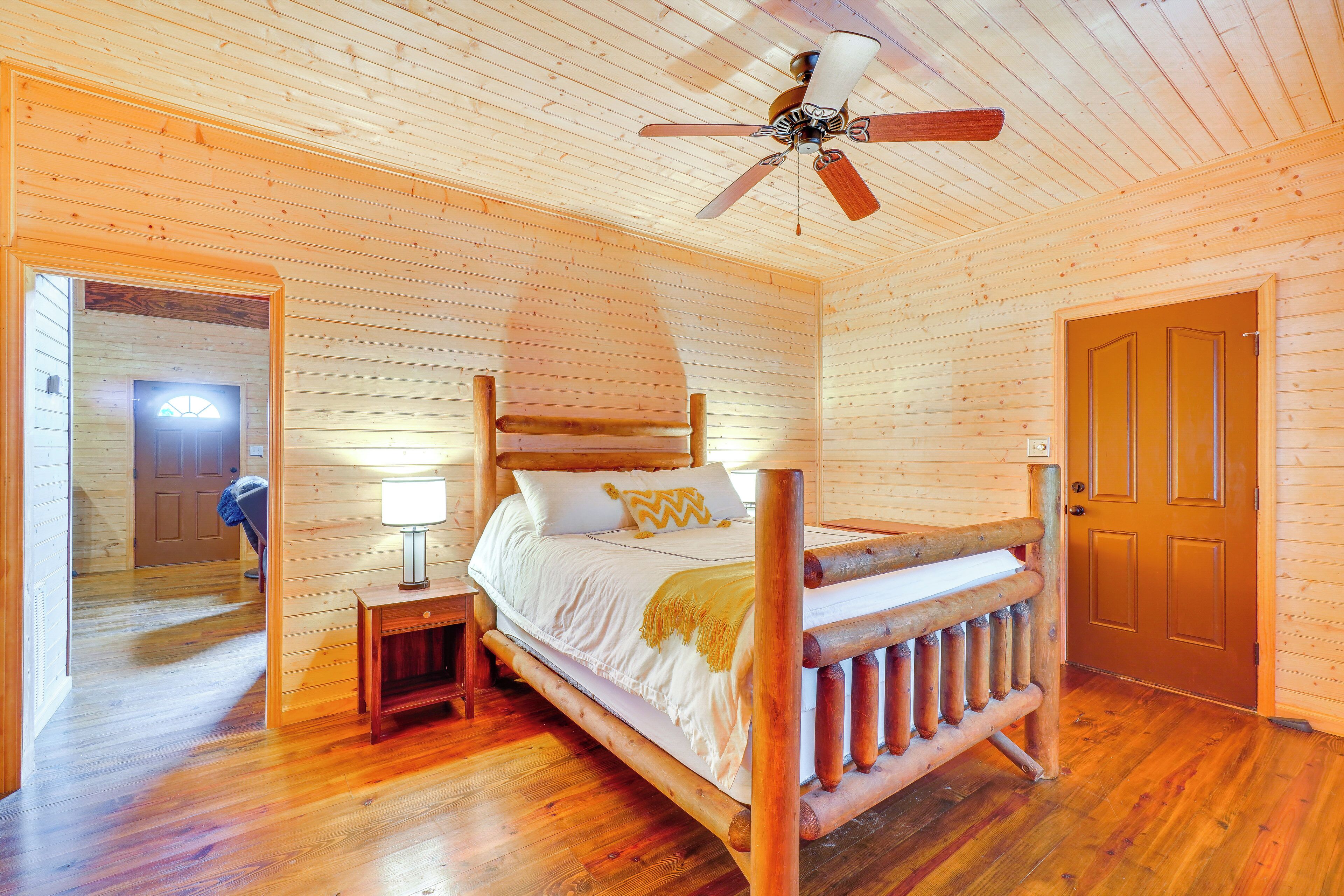 Une chambre dans une cabane en bois, avec un lit, une table de chevet, un ventilateur de plafond et une porte.