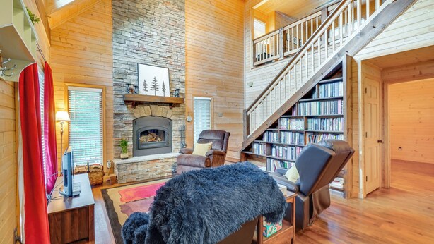 Amplia sala de estar con chimenea, una estantería y una escalera que conduce a un nivel superior.