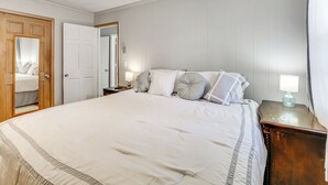 A neatly made bed with a white comforter and pillows, a wooden nightstand with a lamp, and a wooden door with a mirror. - Cozy Mullins Retreat w/ Backyard & Covered Porch! (Mullins)