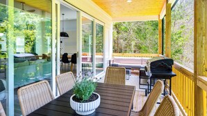 Eine Außenterrasse mit Holzboden, Glas-Schiebetüren, Korbmöbeln, einem Grill und einem Pool, der durch die Glastüren sichtbar ist.