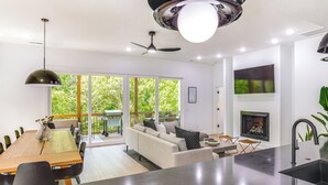 Eine moderne Küche mit einer zentralen Kochinsel, einem Essbereich mit Holztisch und Stühlen, einer Couch und einem Kamin.