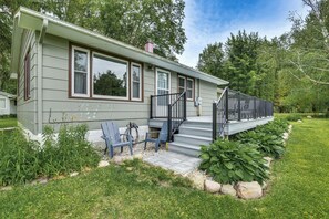 A single-story house with a covered porch, a set of stairs leading to the entrance, and a small garden area with a bench and plants. - Charming Reading Home w/ Lake Views & Private Dock (Reading)