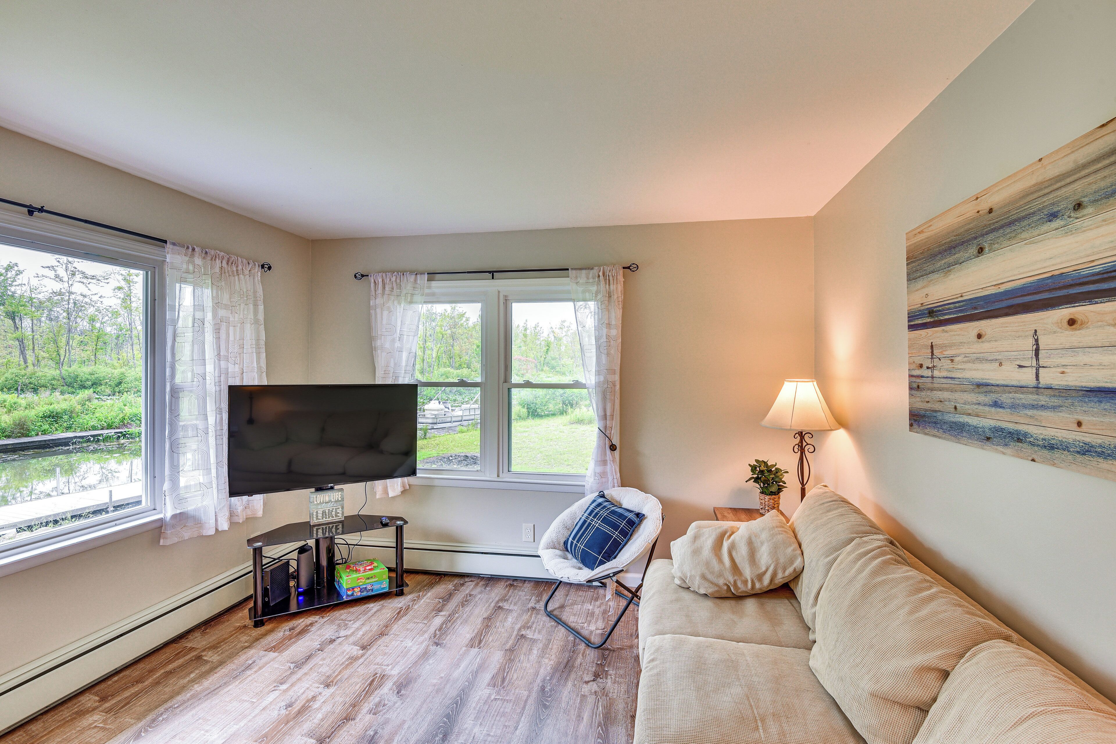 Un salon avec un téléviseur, un canapé, un fauteuil et un tableau accroché au mur.
