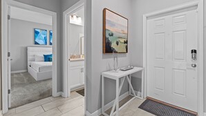 Un couloir avec une porte blanche, une console blanche et un tableau accroché au mur.