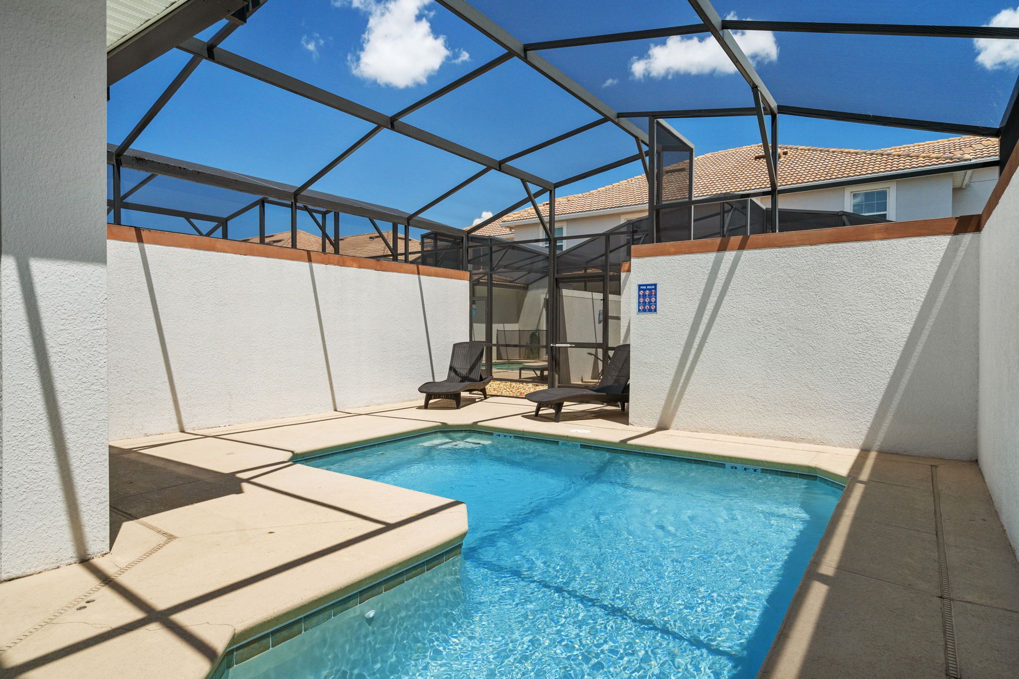 A swimming pool with a glass enclosure and lounge chairs.