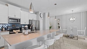 Une cuisine moderne avec des meubles blancs, des appareils en acier inoxydable et un îlot central doté de tabourets de bar.