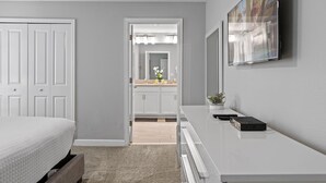 Une chambre à coucher comprenant un lit, une commode, un miroir et un téléviseur fixé au mur.
