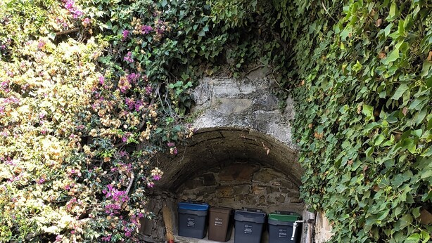 A stone archway with bins and a broom leaning against it.