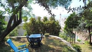 A patio with a table and chairs, surrounded by greenery and a view of buildings in the background.