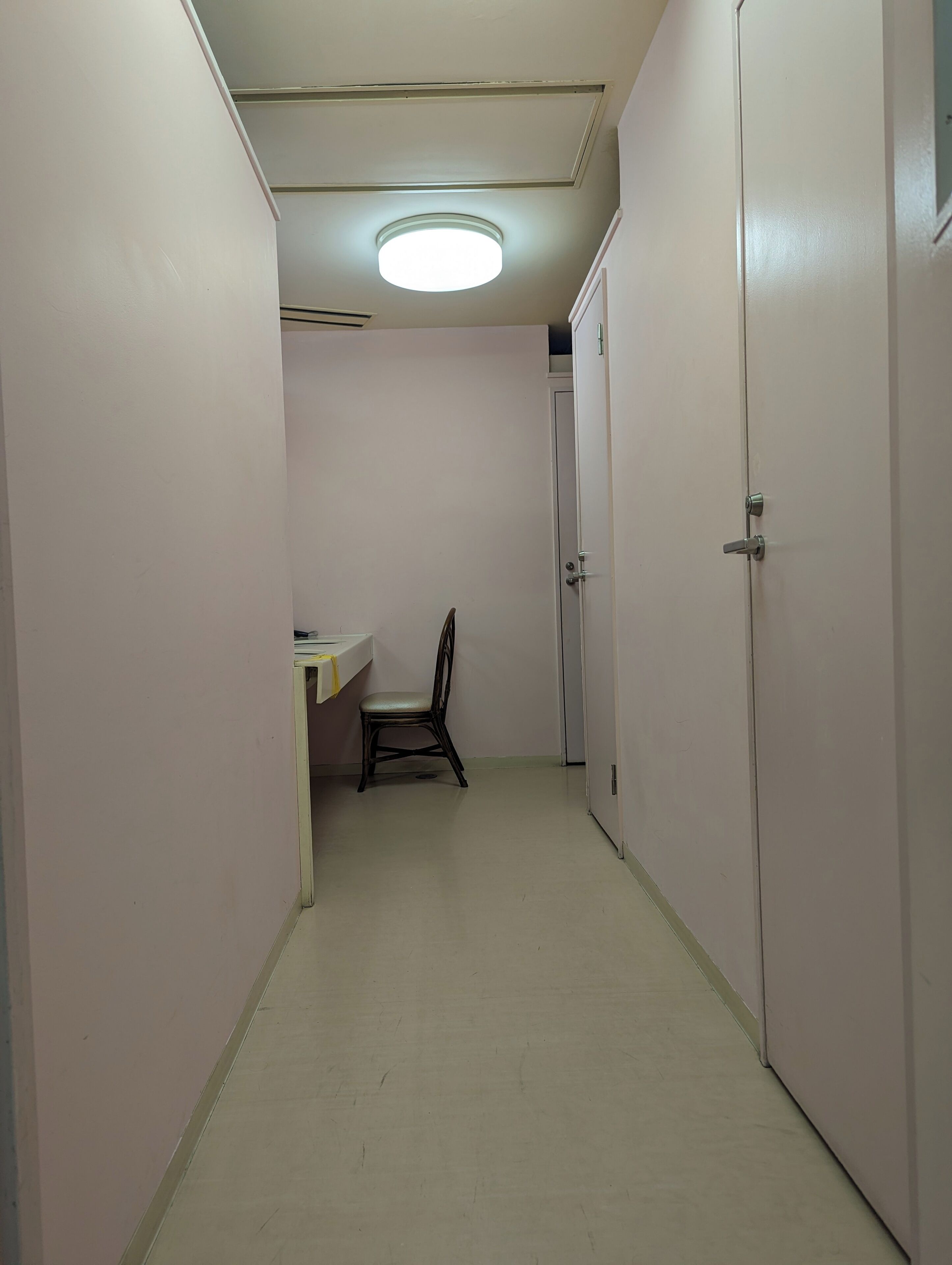 A narrow hallway with a desk and chair, a door on the right, and a ceiling light.
