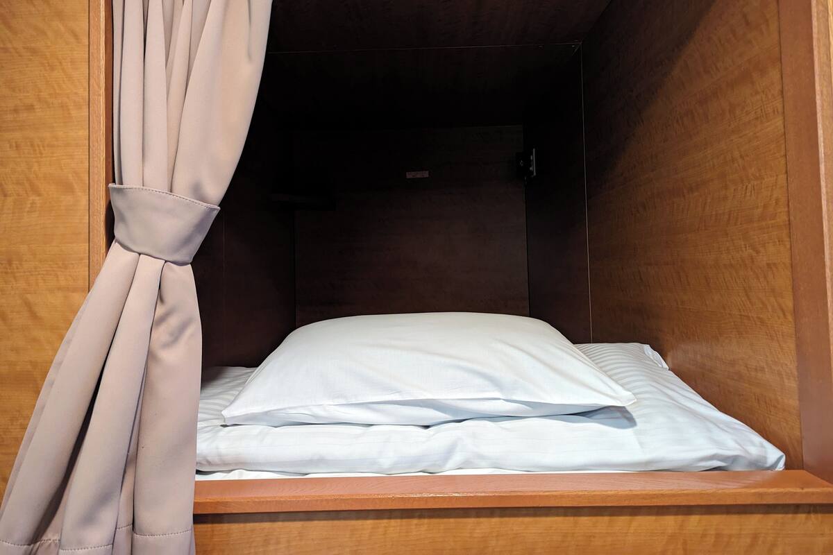 A small, wooden-framed bed with white bedding and a beige curtain.