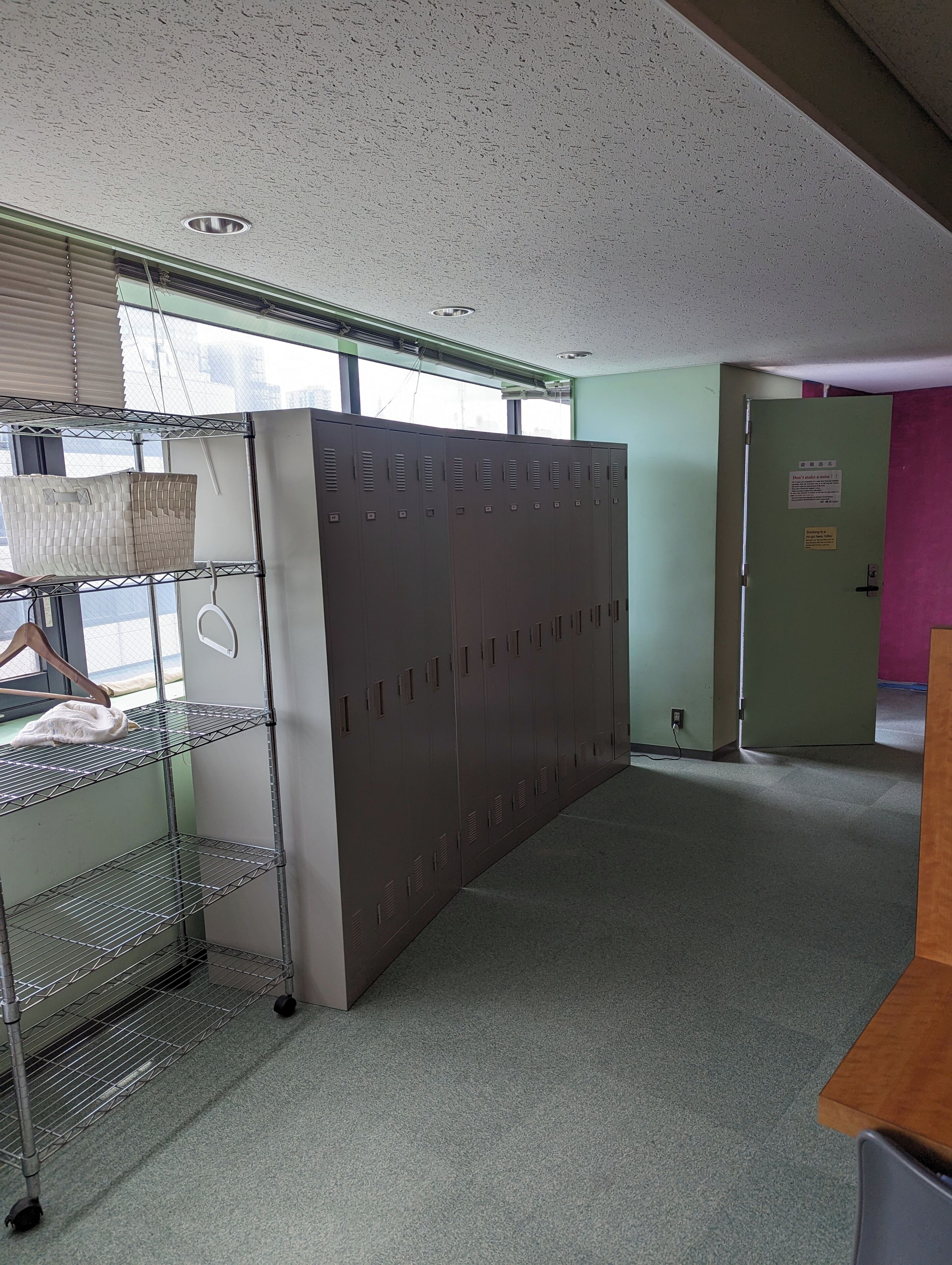 A room with metal lockers, a metal shelf unit, and a door with a sign.