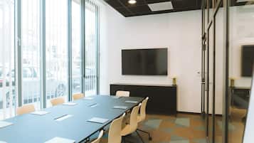 A conference room with a long table, chairs, a flat-screen TV, and large windows.
