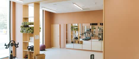 Een fitnessruimte met trainingsapparatuur, een loopband en een spiegelwand.