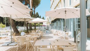 Een terras buiten met witte tafels en stoelen, grote parasols en een houten dek.