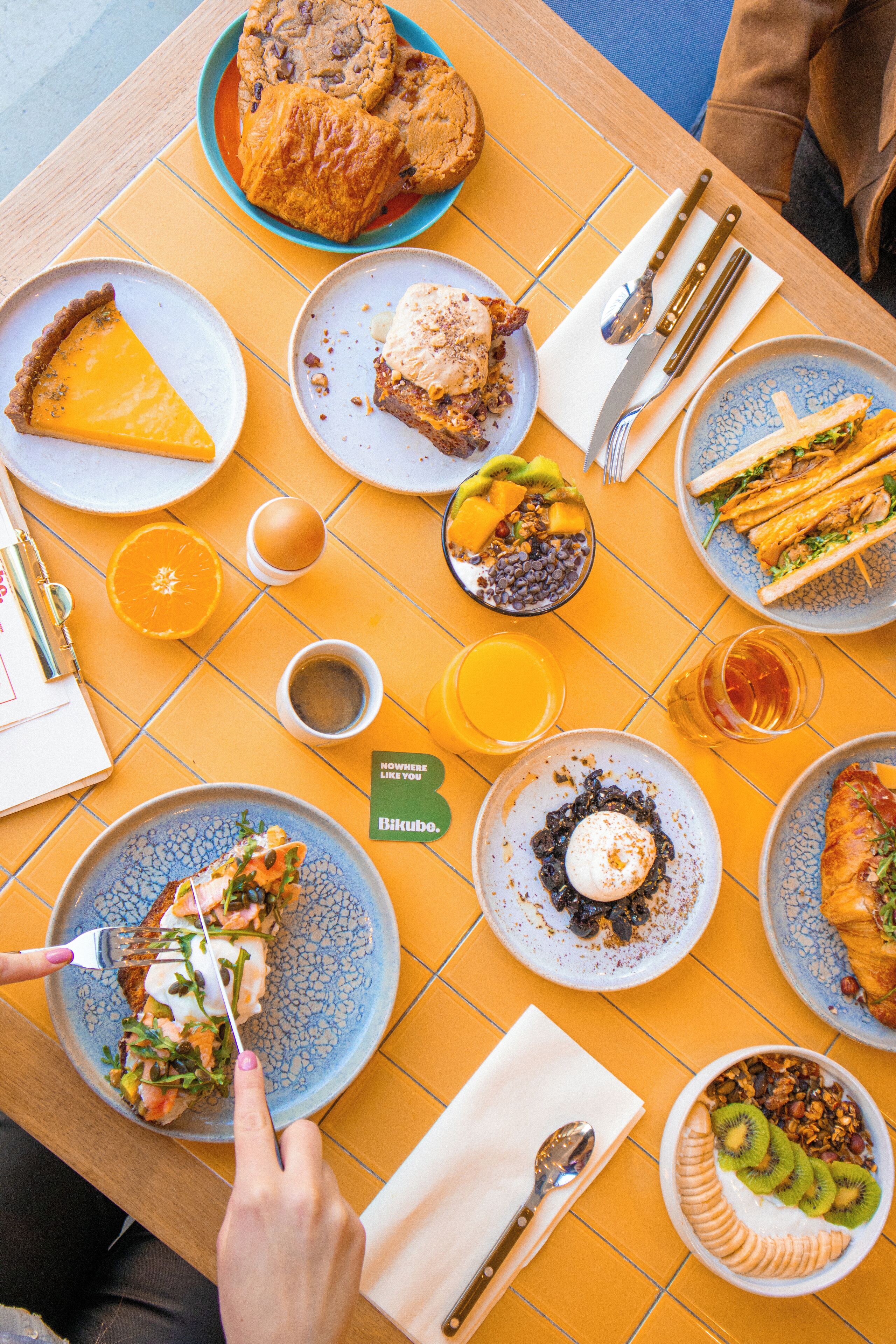A breakfast table with various dishes including a croissant, a slice of pie, and a bowl of fruit.