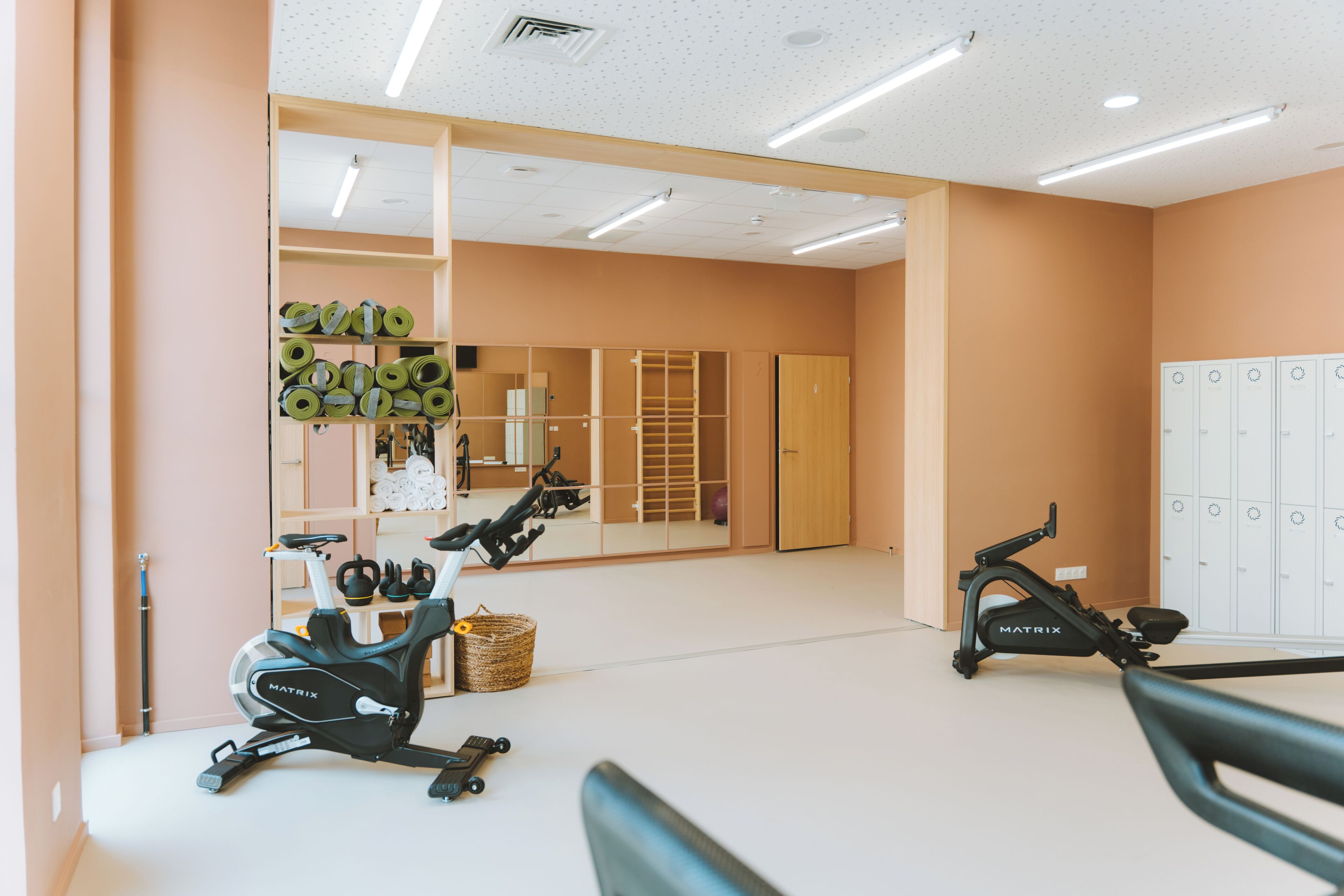 Un gimnasio con bicicletas estáticas, un espejo grande y casilleros.