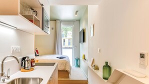 Een kleine hotelkamer met kitchenette, een bed, een televisie en een raam met gordijnen.