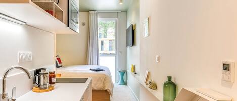 Habitación de hotel compacta con kitchenette, una cama, televisor y ventana con cortinas.