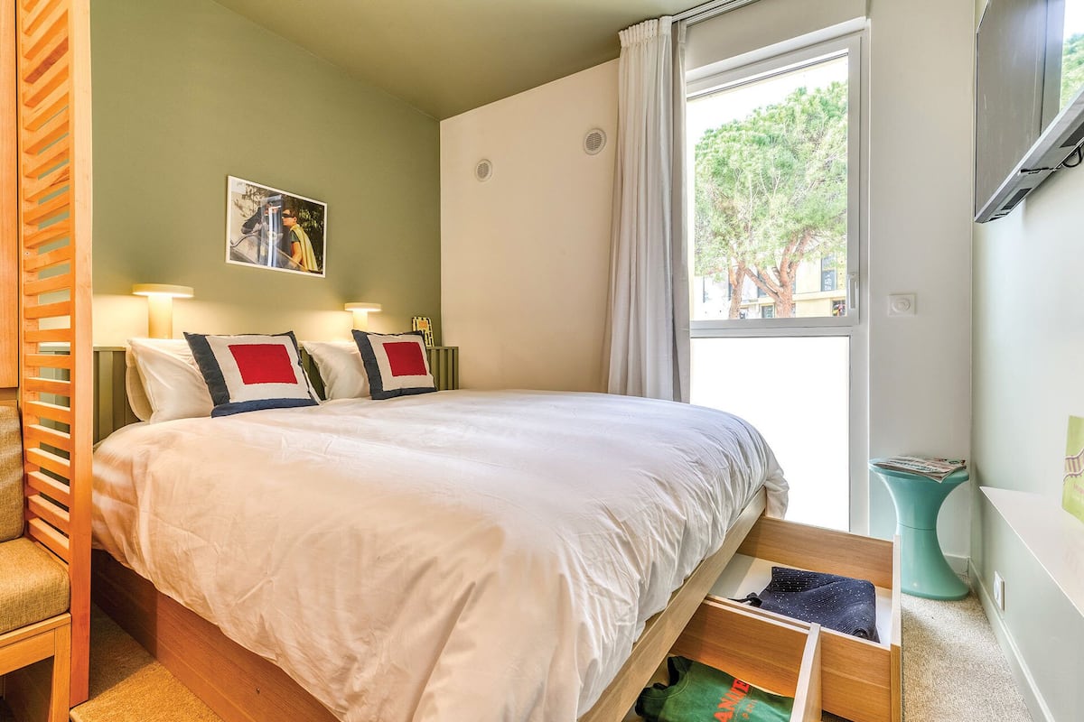 A bedroom with a bed, bedside tables, a window, and a view of trees outside.