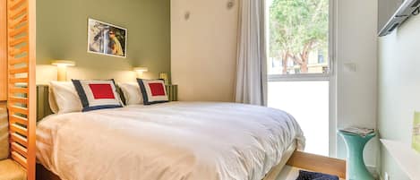 A bedroom with a bed, bedside tables, a window, and a view of trees outside.