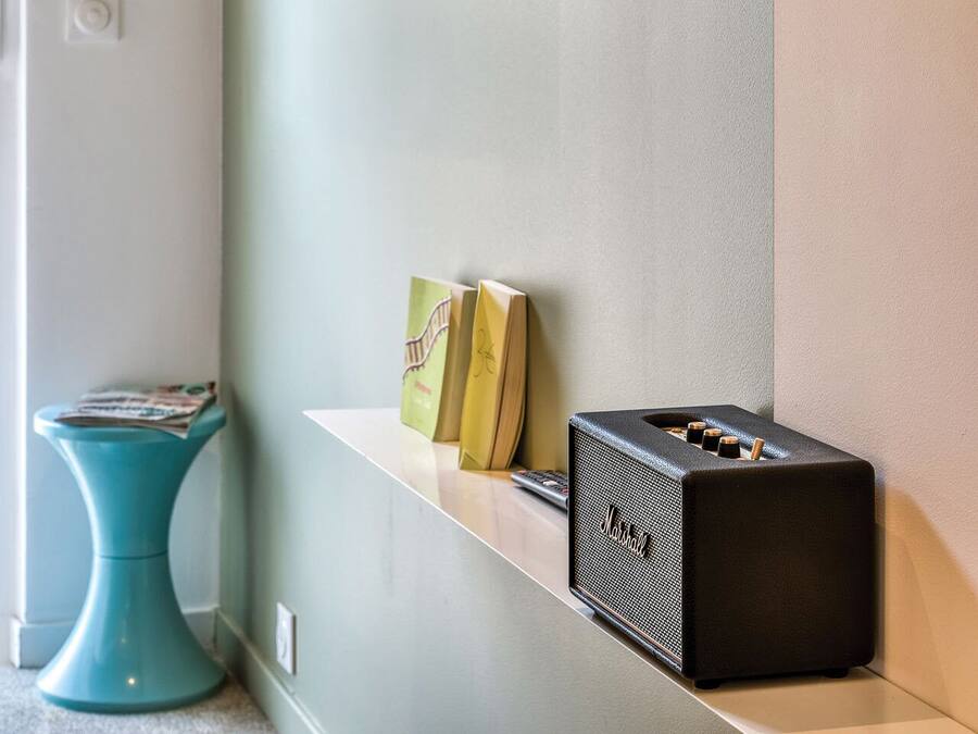 A modern room with a flat-screen TV mounted on the wall, a small shelf with books and a speaker, and a teal-colored side table.