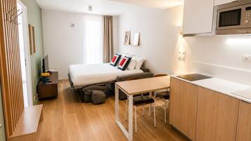 Een compacte hotelkamer met een bed, een klein bureau, een kitchenette en een raam met gordijnen.