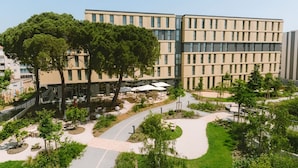 Een modern gebouw met een plat dak, veel ramen en een aangelegde binnentuin met bomen en buiten zitplaatsen.